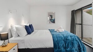 Una habitación de hotel moderna con cama, mesita de noche, lámpara, un cuadro y un ventanal grande.