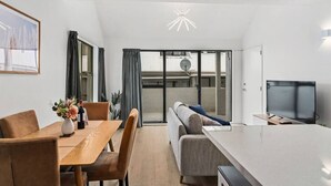 Una sala moderna con una mesa de comedor de madera, asientos cómodos, un sofá grande y un televisor de pantalla plana.