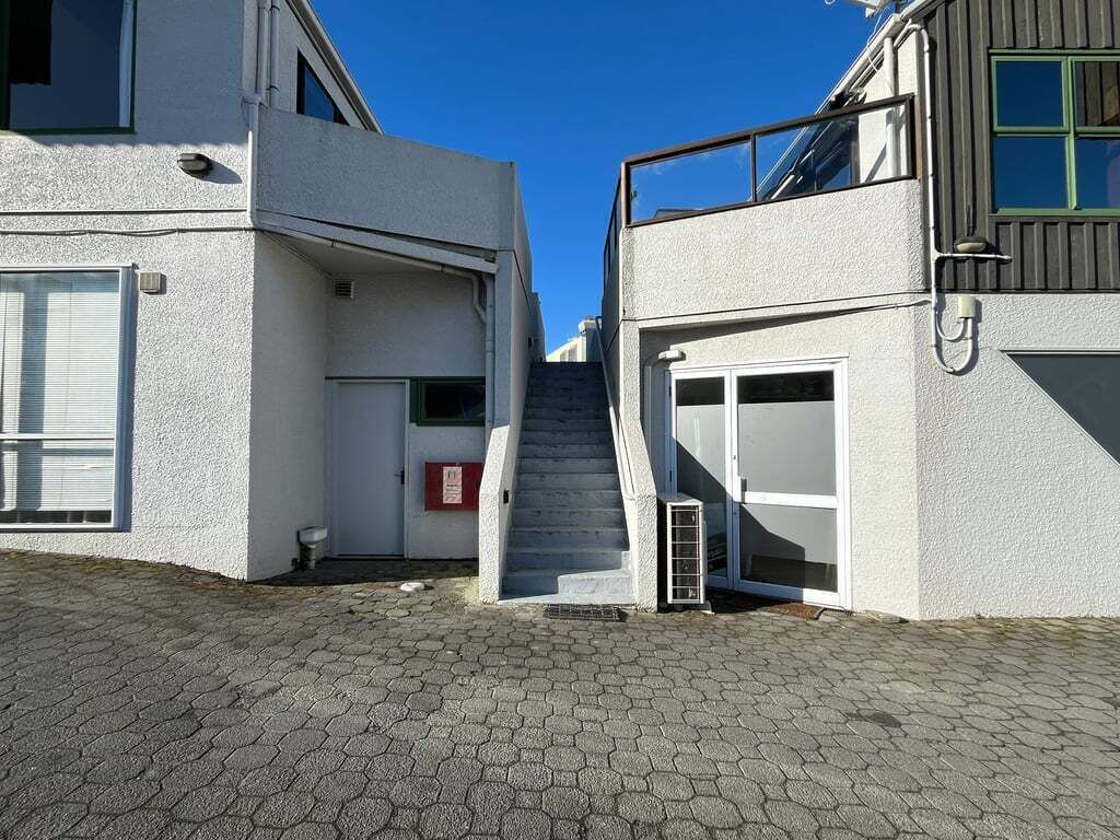 Un edificio a due piani con una scala che conduce al piano superiore, un'autorimessa e un piccolo spazio esterno con un vialetto lastricato.