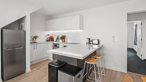 Una cocina moderna con armarios blancos, un refrigerador de acero inoxidable, una isla central con taburetes y un pequeño cubo de basura.