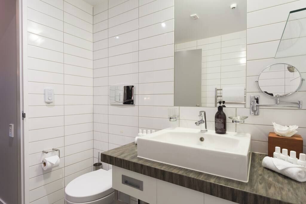 A modern bathroom with white tiled walls, a white sink, a mirror, and a toilet.