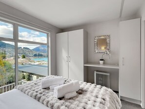 A bedroom with a large window, a bed with white linens, a fur throw, and a radiator. - Spectacular VIEWS, 2 Bedrooms & BIG DECK! (Queenstown)