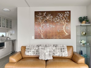 A modern living room with a sofa, a decorative wall piece, and a glass cabinet with items. - Spectacular VIEWS, 2 Bedrooms & BIG DECK! (Queenstown)