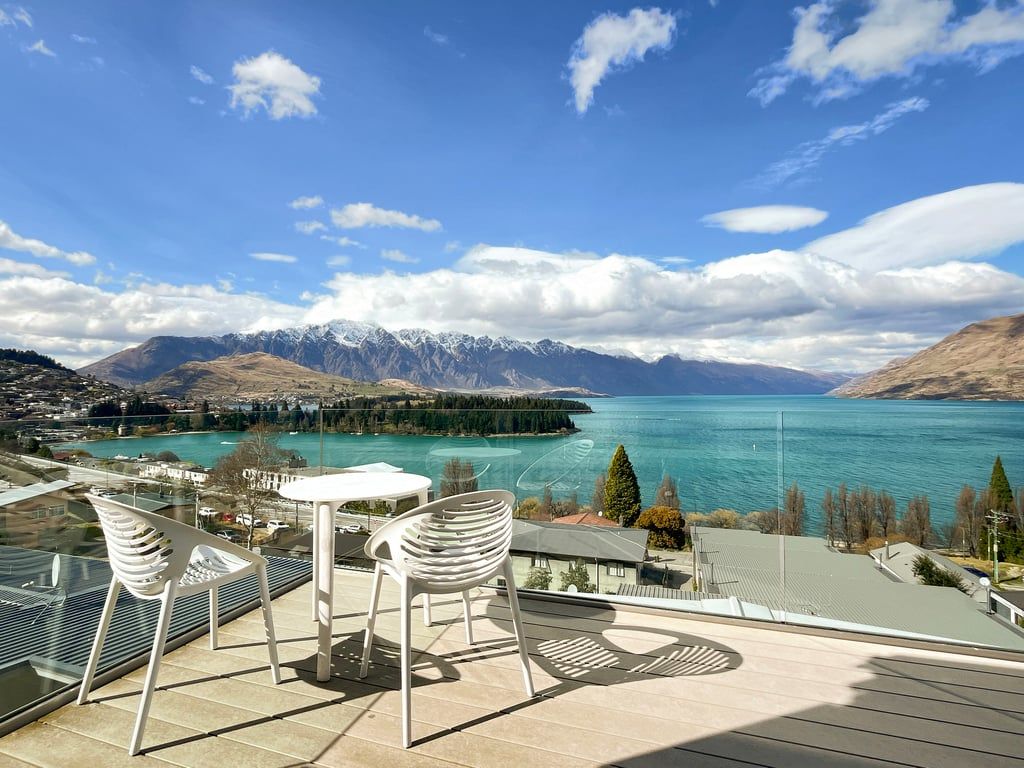A terrace with a table and chairs overlooking a lake with mountains in the background.
