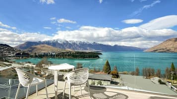 A terrace with a table and chairs overlooking a lake with mountains in the background.