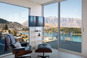 A modern living room with a large window, a flat-screen TV, a sofa, and a small table with chairs.