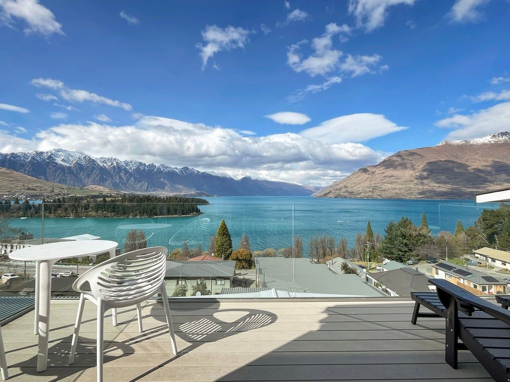 A terrace with a view of a lake and mountains, featuring a table and chairs.