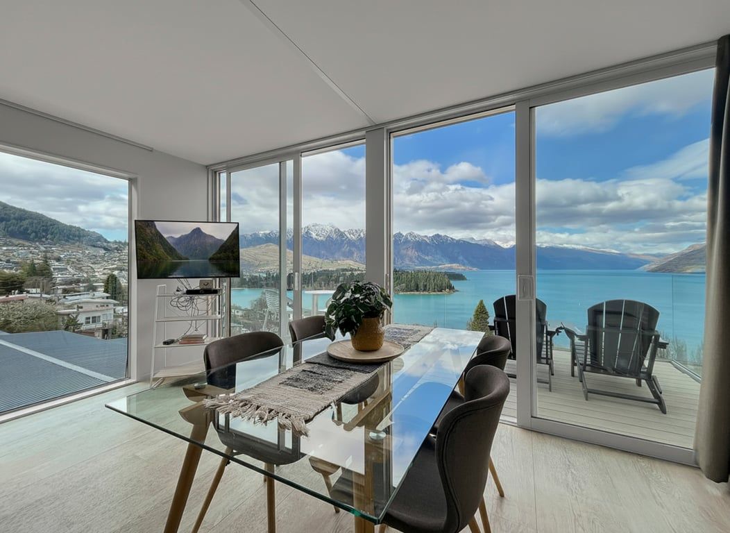 A modern dining area with a glass table, chairs, and a television.