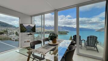 A modern dining area with a glass table, chairs, and a television.