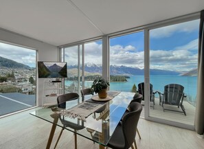 A modern dining area with a glass table, chairs, and a television. - Spectacular VIEWS, 2 Bedrooms & BIG DECK! (Queenstown)