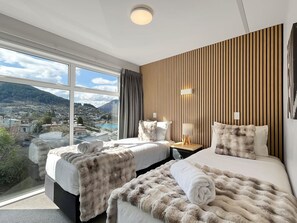 A hotel room with two beds, a large window with a city view, and a wooden panel wall.