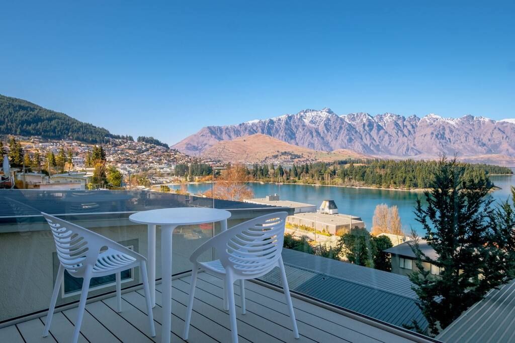 A terrace with two white chairs and a table overlooking a lake and mountains.