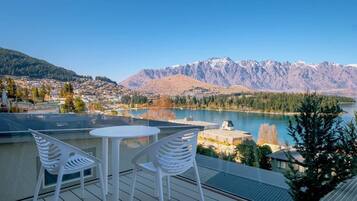 A terrace with two white chairs and a table overlooking a lake and mountains.