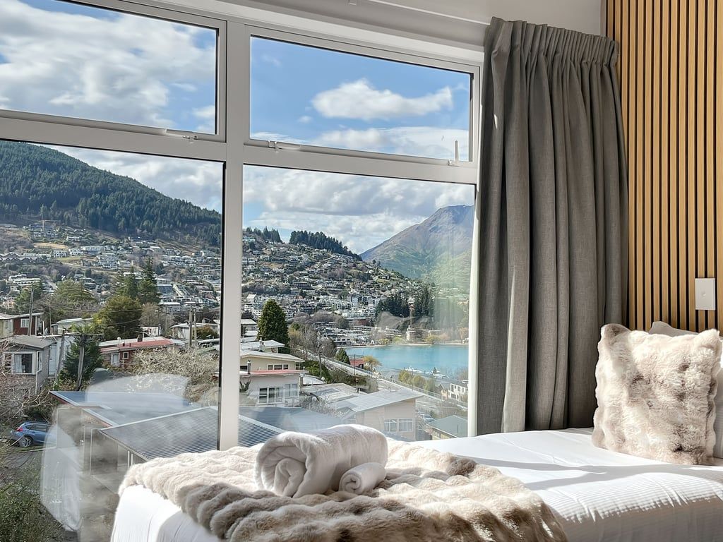 A hotel room with a large window offering a view of a town and mountains.