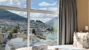 A hotel room with a large window offering a view of a town and mountains.