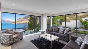 A modern living room with large windows, a sofa, a coffee table, and a view of a lake and mountains.