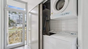 A modern laundry room with a front-loading washer and dryer, a sink, and a window with a view of a grassy area.