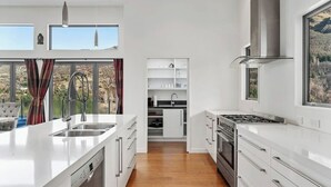 Een moderne keuken met witte kastjes, een roestvrijstalen afzuigkap en een groot kookeiland met een vaatwasser.