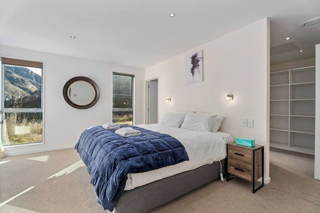A modern bedroom with a large bed, a bedside table, a wardrobe, and a view of the outdoors.