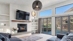 Een moderne woonkamer met een open haard, een flatscreentelevisie en een groot raam met uitzicht op de omgeving.