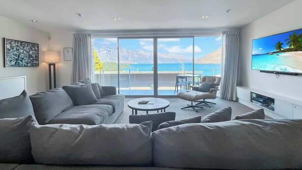 Un salon moderne avec un grand canapé, une table basse et un téléviseur à écran plat fixé au mur. La pièce est dotée d’une porte-fenêtre coulissante qui donne sur un balcon offrant une vue imprenable sur l’océan.