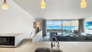 Une cuisine moderne dotée d’un four à micro-ondes encastré, d’un évier en acier inoxydable et d’un coin repas offrant une vue sur la mer.