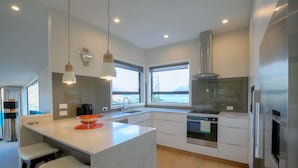 A modern kitchen with a large island, stainless steel appliances, and large windows offering a view.