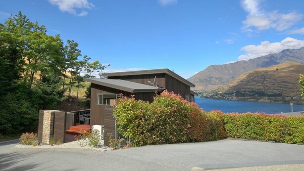 A modern house with a garage, a stone wall, and a view of mountains and a lake.