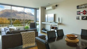 A modern living room with a sofa, a dining table, and a fireplace. - Mountain View 2 Bed Apartment Pounamu 216 (Queenstown)
