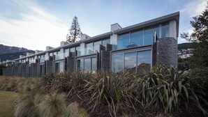 A modern multi-story building with large windows and a stone pillar. - Mountain View 2 Bed Apartment Pounamu 216 (Queenstown)
