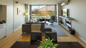 A modern living room with a sofa, chairs, a TV, and a fireplace. - Mountain View 2 Bed Apartment Pounamu 216 (Queenstown)