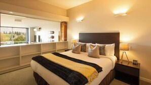A modern bedroom with a large bed, bedside lamps, and a view of a cityscape through a large window. - Mountain View 2 Bed Apartment Pounamu 216 (Queenstown)