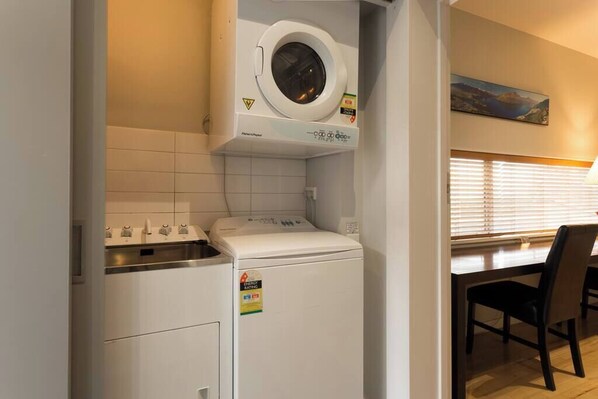 Een praktische wasruimte met een voorlader wasmachine en droger, een klein wastafeltje en een eethoek met tafel en stoelen.