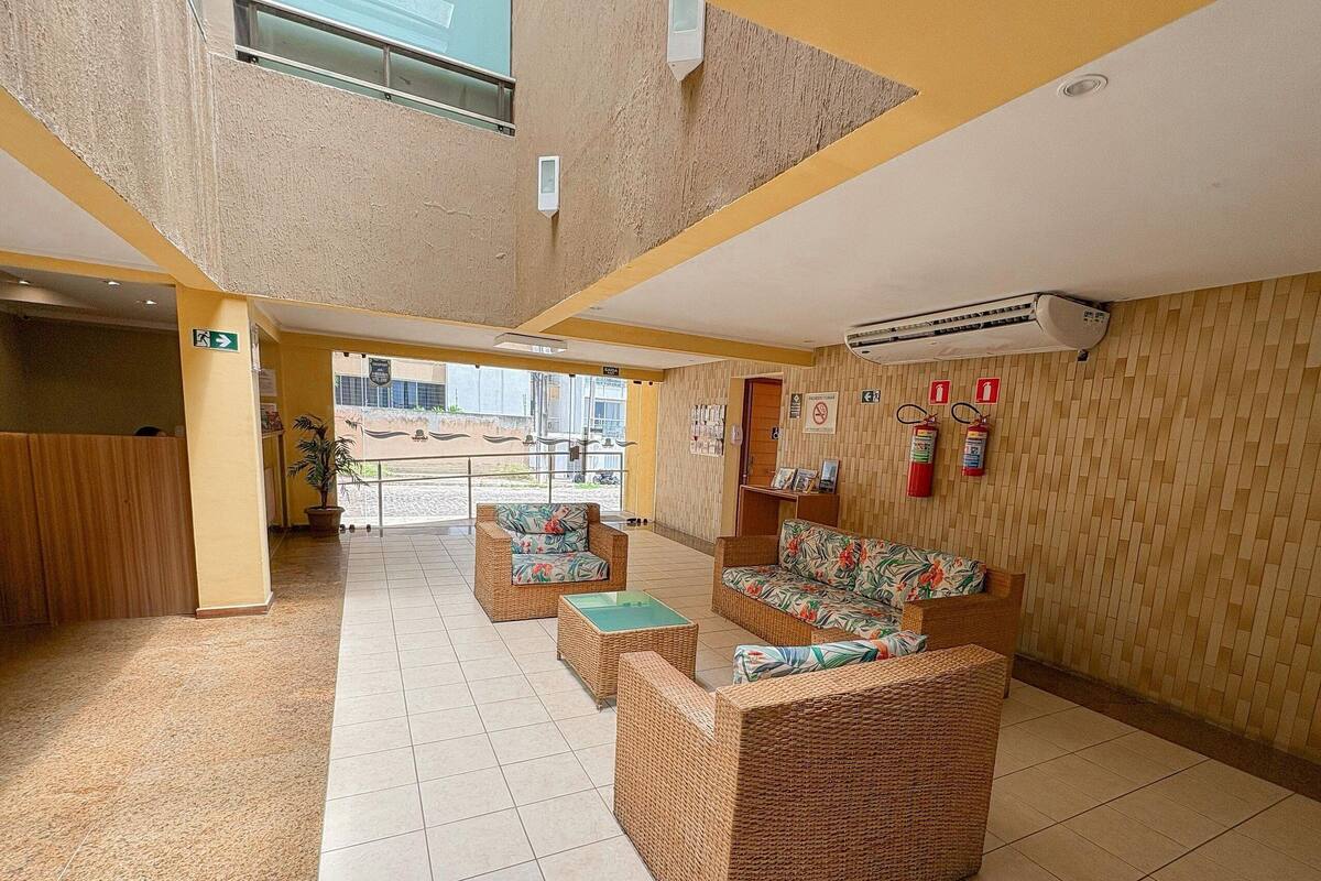Un hall con muebles de mimbre, un extintor y una señal de salida visible.
