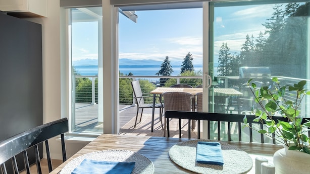 A balcony with a table and chairs, a view of the ocean and mountains, and a potted plant. - Water & Mountain Views: Escape to Whidbey Island! (Freeland)