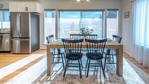 A modern kitchen with a stainless steel refrigerator, a dining table with six chairs, and a chandelier. - Water & Mountain Views: Escape to Whidbey Island! (Freeland)