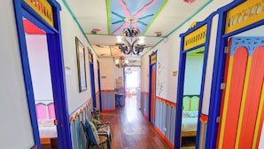 A hallway with wooden flooring and colorful walls, leading to a room with a bed and a chair. - Hostal Mythos (Filandia)