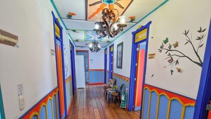 A hallway with colorful walls, a wooden floor, and a ceiling fan. - Hostal Mythos (Filandia)