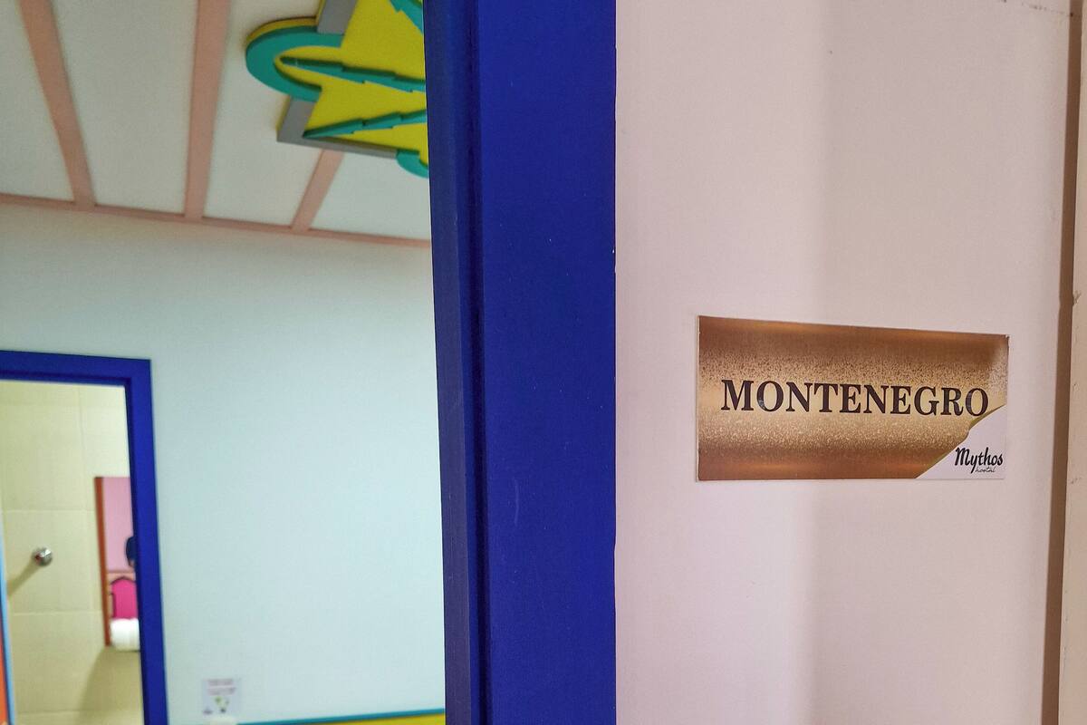 Una habitación con una cama, una puerta con la leyenda 'MONTENEGRO' y un baño con inodoro y lavamanos.