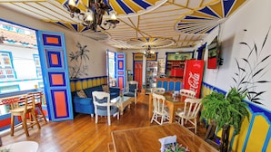 A vibrant room with a wooden floor, a sofa, a dining table with chairs, a refrigerator, and a ceiling fan. - Hostal Mythos (Filandia)