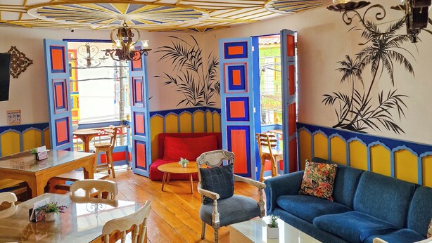 A vibrant room with a wooden floor, a blue sofa, a wooden dining table, and a red couch. - Hostal Mythos (Filandia)