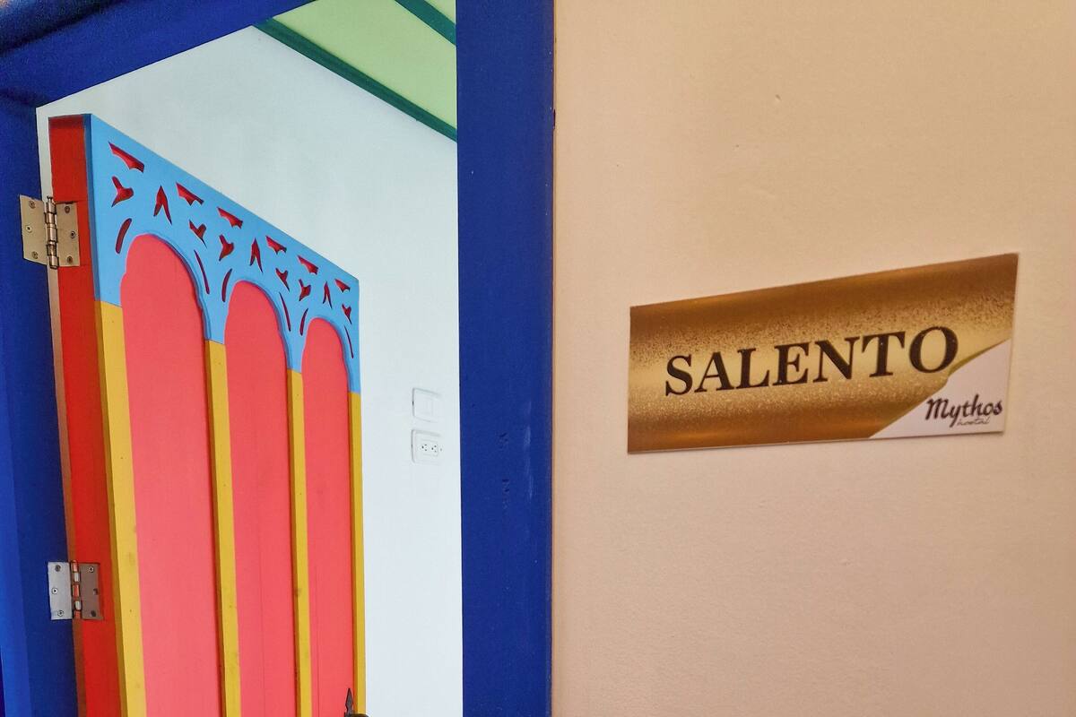 Una habitación con una cama, una puerta con rayas de colores y una pared con una placa que dice 'SALENTO'.