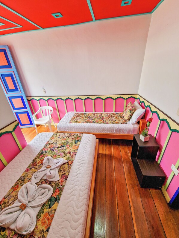 A room with two beds, wooden flooring, and a chair. - Hostal Mythos (Filandia)