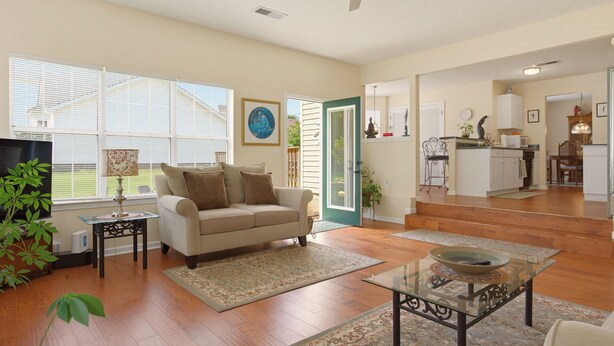 A living room with a sofa, coffee table, and a TV. There are wooden floors, a window with blinds, and a door leading to a kitchen. - World Cup Work Base -Large Home + OFFICE- Sleeps 8 (Stonecrest)