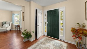 A spacious entryway with a dark green door, a white door, and a beige wall. There is a white chair and a small table with a plant. - World Cup Work Base -Large Home + OFFICE- Sleeps 8 (Stonecrest)