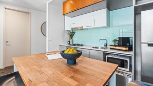Une cuisine moderne avec une table en bois, un saladier de fruits et des appareils électroménagers en acier inoxydable.