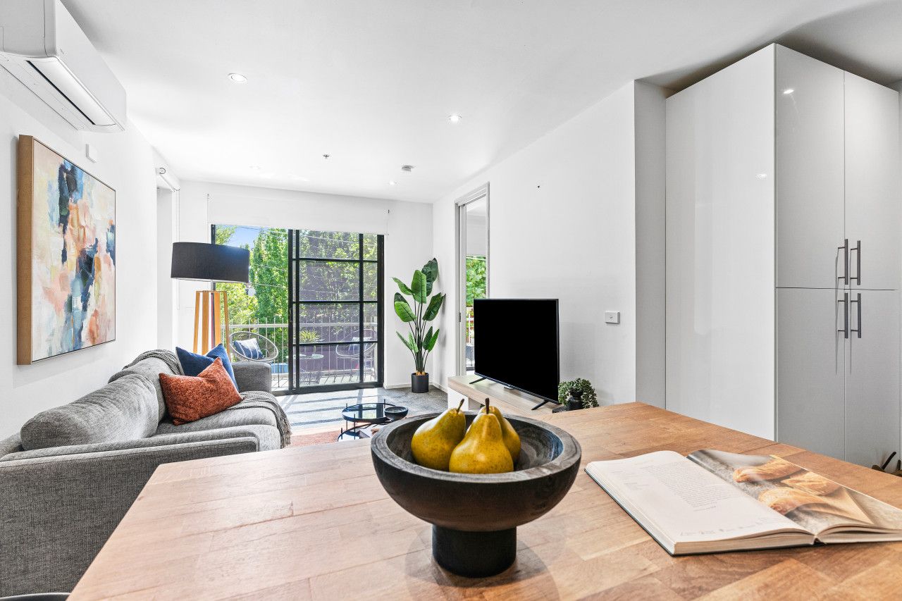Ein modernes Wohnzimmer mit einem grauen Sofa, einem Holzesstisch, einer schwarzen Schüssel mit Birnen und einem Fernseher.
