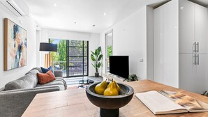 Un salon moderne avec un canapé gris, une table à manger en bois, un saladier noir contenant des poires et un téléviseur.