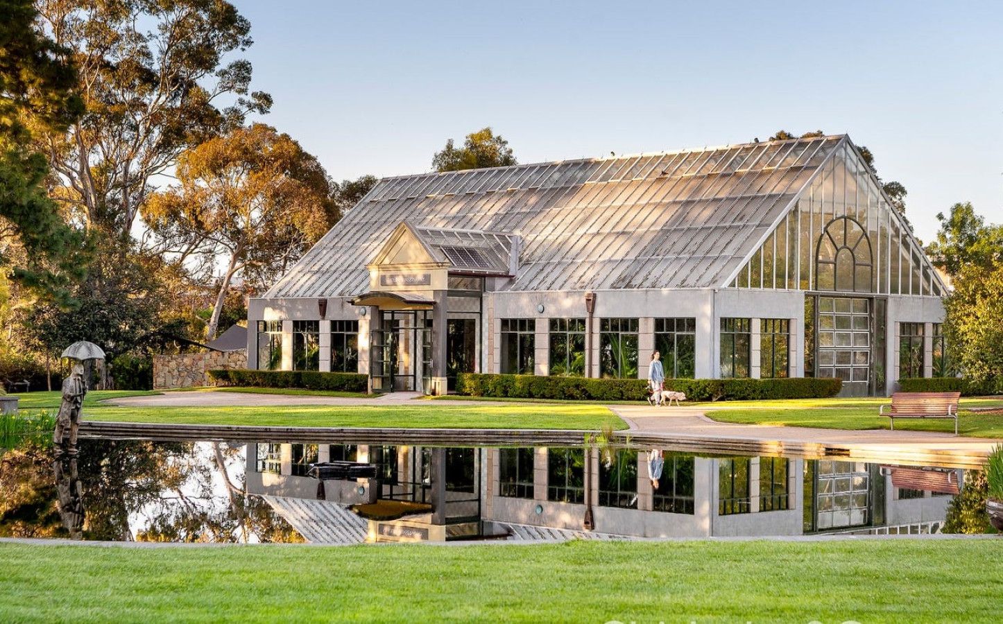 A large greenhouse-style building with a reflective pond in front.