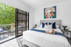 A modern bedroom with a large bed, a balcony with outdoor furniture, and a large window.